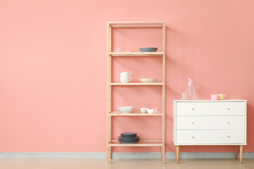Shelving unit and chest of drawers with dishes near pink wall
