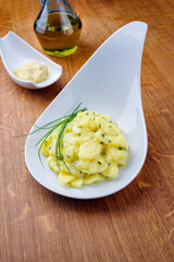 Traditioneller deutscher Kartoffelsalat mit Zwiebel und Schnittlauch serviert als close-up in einer Design Schale auf einem Design Holz Board