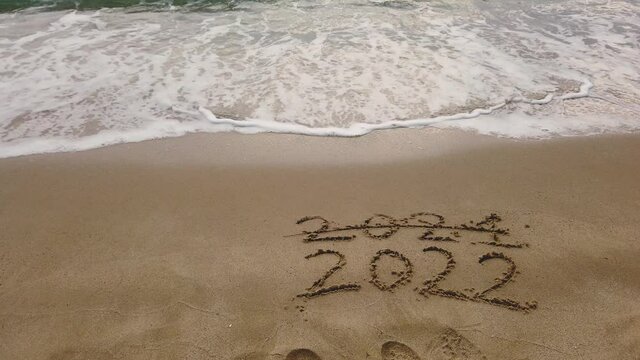 NEW YEAR WRITING 2022 AND ENDING 2021 WITH CROSSOUT ON THE BEACH SAND