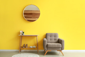 Soft armchair and stand with shoes near yellow wall