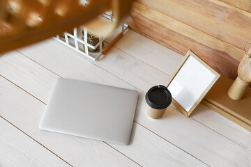 Modern workplace with laptop, frame and cup of coffee near wooden wall