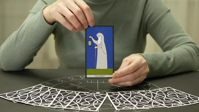 Adult woman shows tarot card. Hands of fortune teller woman open and hold THE HERMIT card on table with altar of tarot. Forecasting concept.