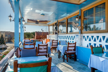Interior of a fish restaurant open terrace decorated in a blue colour. Spacious restaurant hall is empty, there are no visitors at the tables. Terrace offers city views