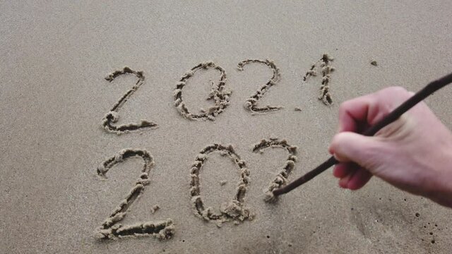 NEW YEAR WRITING 2022 AND ENDING 2021 WITH CROSSOUT ON THE BEACH SAND