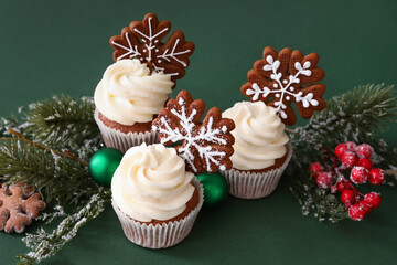 Tasty Christmas cupcakes with gingerbread cookies and decor on green background