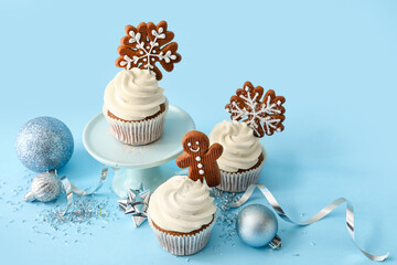 Stand of tasty Christmas cupcakes with gingerbread cookies on blue background