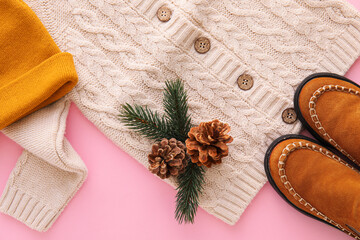 Knitted sweater, hat, shoes and winter decor on color background, closeup