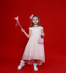 Cute little girl in a pink fairy costume with wings and a magic wand on a red background.