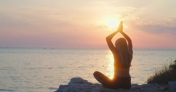 Young women are doing yoga in summer sunset with sea background. Warm-up, healthy life, relaxing and outdoor exercise. Health care, authenticity, sense of balance and calmness.