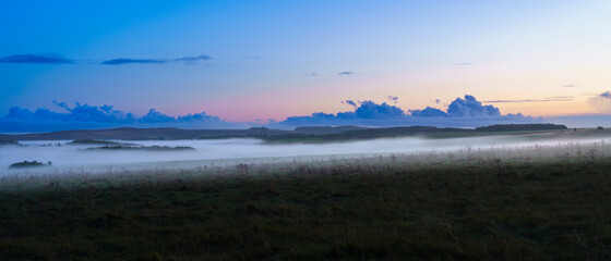 a blanket of ground fog rolling across meadows and woodland in the valley with a red, pink, orange and blue sunset sky, Wiltshire UK