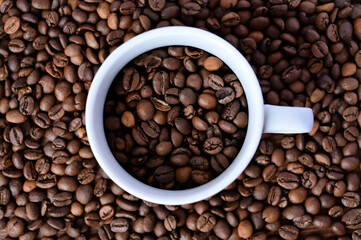 white cup with coffee beans on a coffee background. Close-up. Flat layout with top view