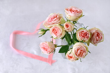 beautiful bouquet of white roses with delicate pink hue and  heart of satin pink ribbon on white silk background. Valentine's day. Selective focus