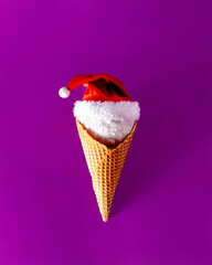 Ice cream cone with a snowball and Santa's hat. On purple background. Creative Christmas or New Year festive concept.Flat lay. 