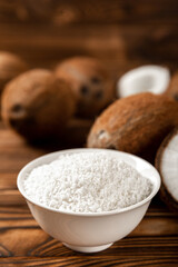 Coconut flakes in a bowl, coconuts on a wooden background. Close-up.