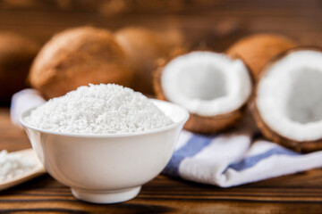 Coconut flakes in a bowl, coconuts on a wooden background. Close-up.