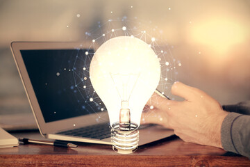 Double exposure of man's hands holding and using a digital device and bulb hologram drawing. Idea concept.