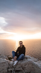 Fototapeta premium person sitting on the clif during sunset dingli window