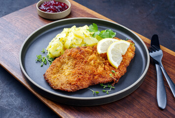 Traditionelles frittiertes Schnitzel mit Kartoffelsalat und Preiselbeeren serviert als close-up auf einem Modern Nordic Design Teller