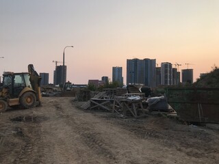 an asphalt paver is driving against the backdrop of new houses in the microdistrict. the tractor goes to the construction site and carries construction waste