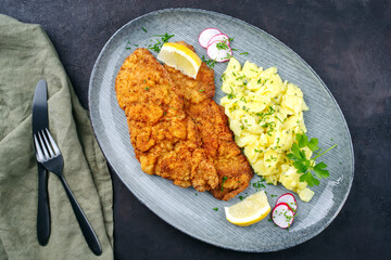 Traditional deep-fried schnitzel with potato salad and lemon slices served as close-up on a modern...