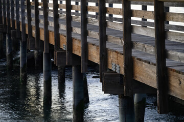 Fototapeta premium abstract diagonal view of a wooden footbridge over water with rows of wooden railings and rusty piers