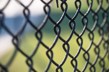 abstract closeup on a rusty chain link fence against a green and blue background with selective focus on one link surrounded by a repeating pattern of blurred links at a slight diagonal