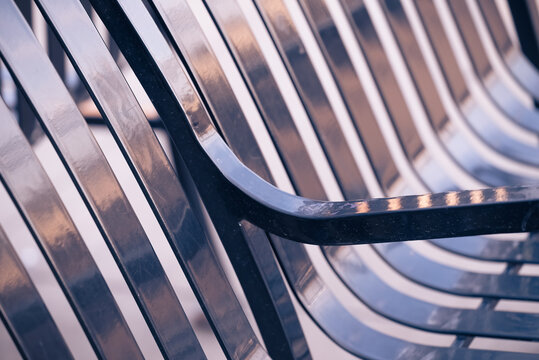 abstract view of a black public park bench reflecting sunset tones with focus on arm rest, repeating diagonal stripe pattern, and detailed metallic texture