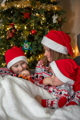 three children have fun on the background of the Christmas tree. children are dressed in New Year's pajamas and santa hats. selektiver fokus