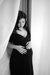 a attractive pregnant woman in a black dress by the window