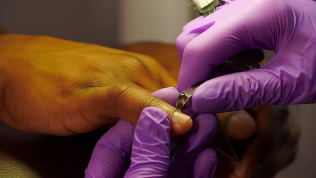 Cuticle circumcision on a afro man finger close-up using manicure tools in a beauty salon. The manicurist does the treatment of the black arms of a male client. Modern body care in a pandemic covid19.