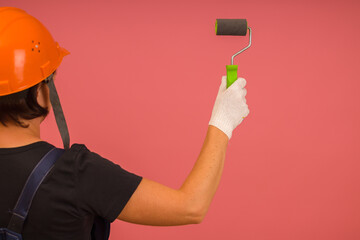 woman paints with roller on pink background