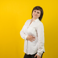 woman in a white shirt put her hand on her stomach on a yellow background