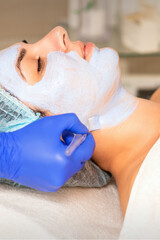 Naklejka premium Face peeling at the beautician. Facial treatment. The beautician applies a cleansing face mask to the female patient