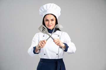 Housewife female chef cook or baker in uniform crossing kitchen appliances isolated on grey wall...