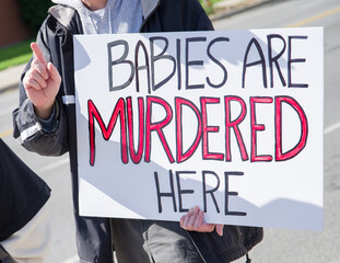 person holding an abortion protest sign that says BABIES ARE MURDERED HERE