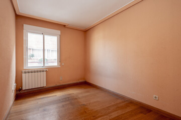 Empty room painted in reddish cream color with oak wood floor with aluminum window and radiator