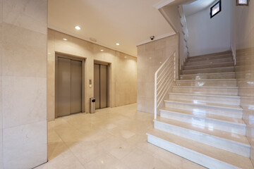 Entrance portal to a building with cream marble floors and walls, stairs and metal elevators