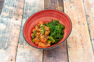 Red tuna and avocado tartare with wakame seaweed salad with sesame seeds and poppy on wooden table