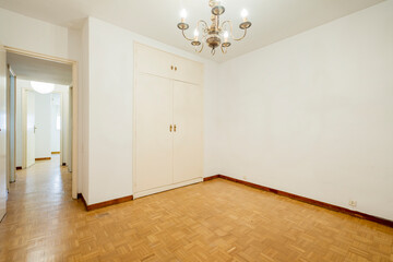 Empty room with built-in wardrobe with large lamp and parquet floors