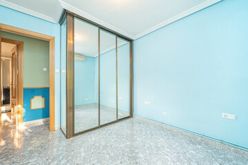 Empty apartment room with built-in wardrobe with large mirrored doors and marble-look floors