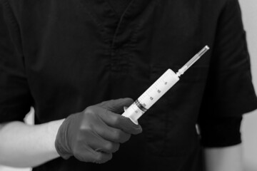 Large white syringe close-up in the hand of a doctor in a sterile glove. Selective focus. Black and white photo.
