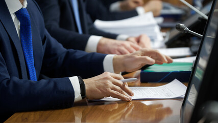 Hands of men - politicians, officials, businessmen or lawyers, sitting at a table with documents,...