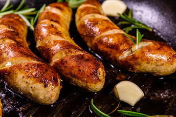 Roasted sausages with rosemary twigs and garlic in a cast iron grill pan
