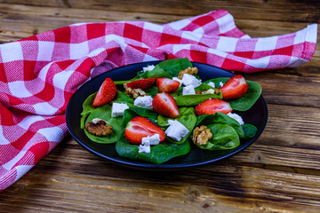 Salad with spinach leaves, feta cheese, walnuts and strawberry on a black plate