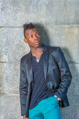 Obraz premium Dressing in a black blazer, green pants, a young black guy with mohawk hair is leaning against the wall, looking up..