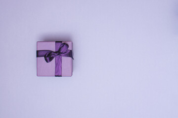 Purple gift box with ribbon on pastel purple background with copy space. Creative realistic minimal gift for Christmas or Holiday giving.