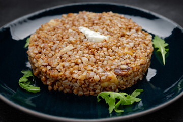 Buckwheat porridge with butter and herbs on a plate, on a dark background