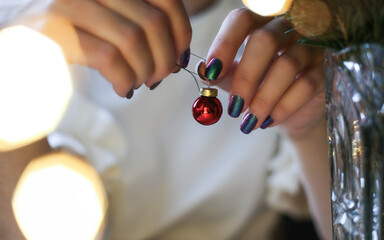 Close up of female hands with trendy green manicure decorating Christmas tree with cute red ball. Copy space for message. Festive postcard or poster. 