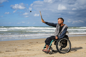 Disabled man sitting on a wheelchair playing paddle ball on the beach