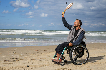 Disabled man sitting on a wheelchair playing paddle ball on the beach